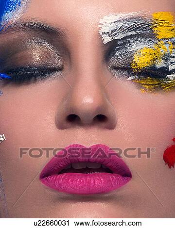 Stock Image - Studio portrait of woman with close eyes and abstract painted face, close up. Fotosearch