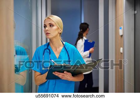 Picture - Surgeon looking through window in hospital, holding clipboard. Fotosearch