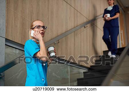 Surgeon using smartphone, holding coffee cup, colleague walking down stairs in background View Large Photo Image Stock Photo - Surgeon using smartphone, holding coffee cup, colleague walking down stairs in background. Fotosearch