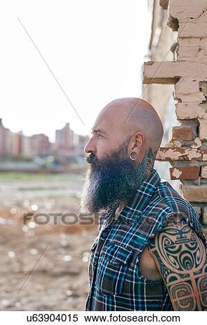Stock Photography - Tattooed mature male hipster by wall of demolished building. Fotosearch