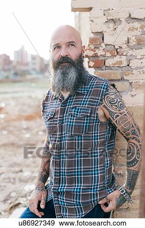 Tattooed mature male hipster leaning against wall of demolished building View Large Photo Image Stock Photo - Tattooed mature male hipster leaning against wall of demolished building. Fotosearch