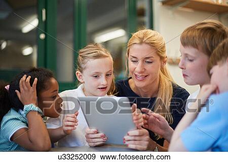 Teacher with schoolboys and girls looking at digital tablet in classroom at primary school View Large Photo Image Stock Photo - Teacher with schoolboys and girls looking at digital tablet in classroom at primary school. Fotosearch