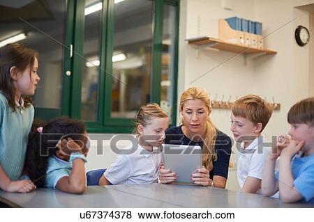 Teacher with schoolboys and girls looking at digital tablet in classroom at primary school View Large Photo Image Stock Photo - Teacher with schoolboys and girls looking at digital tablet in classroom at primary school. Fotosearch
