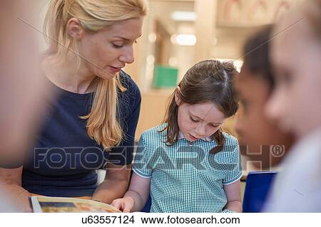 Picture - Teacher with schoolgirls reading storybook in classroom at primary school. Fotosearch