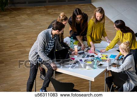 Stock Image - Team of male and female designers discussing colour swatches on design studio table. Fotosearch