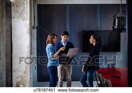 Three businesspeople standing in meeting room, businessman using laptop View Large Photo Image Stock Image - Three businesspeople standing in meeting room, businessman using laptop. Fotosearch