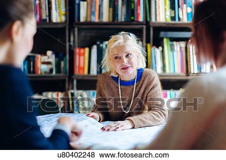 Stock Photo - Three businesswomen, sitting around table, looking through documents. Fotosearch