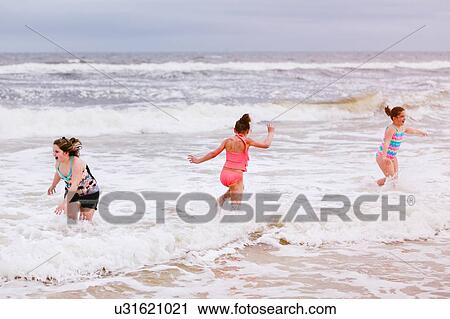 Stock Image - Three girls playing in ocean waves, Dauphin Island, Alabama, USA. Fotosearch