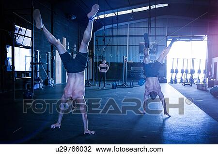Three people exercising in gym, two men doing handstand walks View Large Photo Image Stock Image - Three people exercising in gym, two men doing handstand walks. Fotosearch