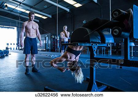 Stock Photograph - Three people exercising in gymnasium, using equipment. Fotosearch