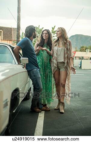 Stock Photography - Three young adults, standing beside car, talking. Fotosearch