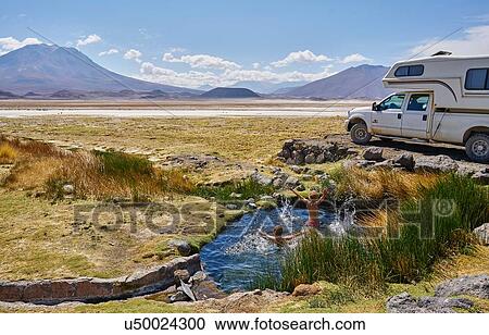 Stock Image - Two boys playing in water pool beside parked recreational vehicle, Salar de Chiguana, Chiguana, Potosi, Bolivia, South America. Fotosearch