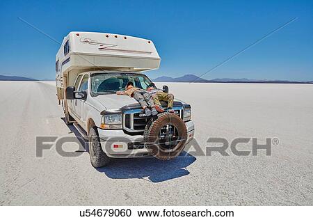 Stock Image - Two boys relaxing on parked recreational vehicle, Salar de Uyuni, Uyuni, Oruro, Bolivia, South America. Fotosearch