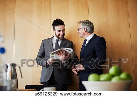 Two businessman chatting and reading newspaper in office boardroom View Large Photo Image Stock Photo - Two businessman chatting and reading newspaper in office boardroom. Fotosearch