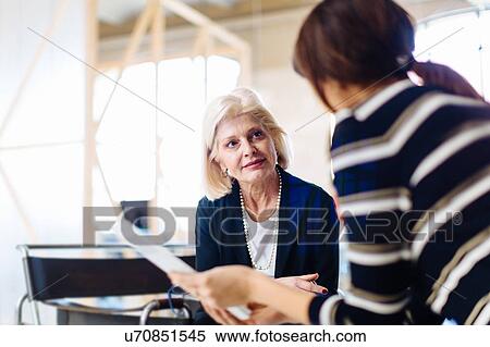 Stock Photography - Two businesswomen in meeting, woman in foreground holding document. Fotosearch