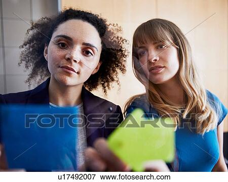 Stock Photo - Two businesswomen looking at ideas on sticky notes. Fotosearch