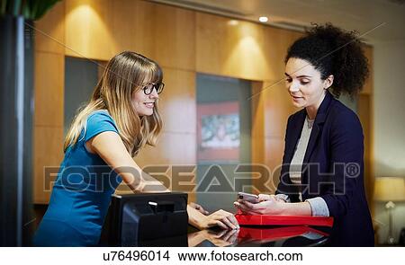 Picture - Two businesswomen looking at smartphone in office reception. Fotosearch