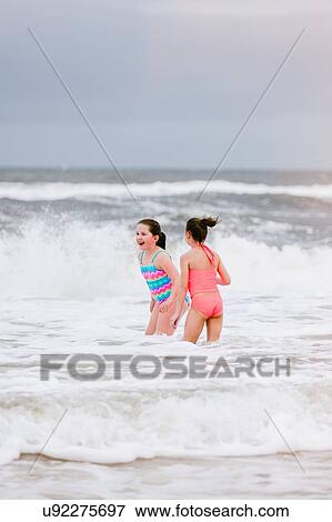 Stock Photo - Two girls standing in ocean waves, Dauphin Island, Alabama, USA. Fotosearch