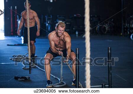 Stock Photography - Two men exercising in gymnasium, sled training. Fotosearch
