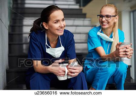 Stock Photograph - Two surgeons taking a break, sitting on steps, holding coffee cups, smiling. Fotosearch