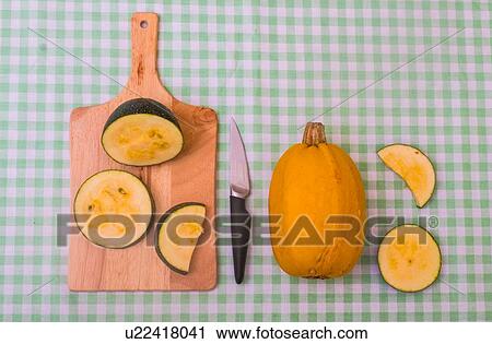 Stock Image - Two varieties of squash, one whole, the other sliced on chopping board, elevated view. Fotosearch
