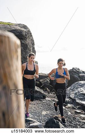 Stock Image - Two young female runners running on rocky beach, Las Palmas, Canary Islands, Spain. Fotosearch