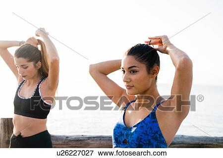 Two young women training on beach, tying hair ponytails View Large Photo Image Stock Photo - Two young women training on beach, tying hair ponytails. Fotosearch