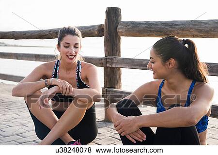 Two young women training on waterfront, sitting chatting View Large Photo Image Stock Photo - Two young women training on waterfront, sitting chatting. Fotosearch