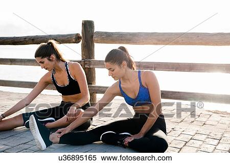 Stock Photography - Two young women training on waterfront, touching toes. Fotosearch