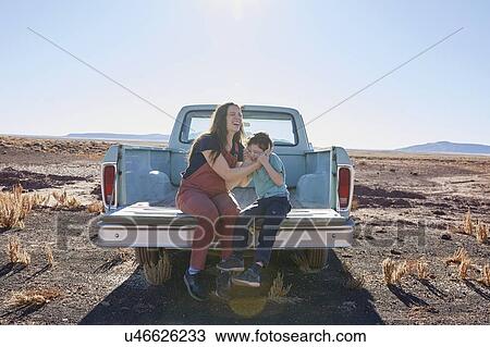 Stock Image - USA, Arizona, Mother with son (6-7) sitting on tailgate of pick-up truck. Fotosearch
