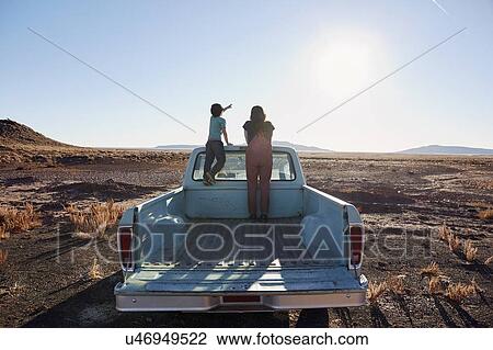 Stock Image - USA, Arizona, Mother with son (6-7) standing on pick up truck parked in desert landscape. Fotosearch