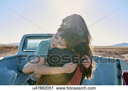 Stock Image - USA, Arizona, Mother with son (6-7) embracing on pick up truck parked in desert landscape. Fotosearch