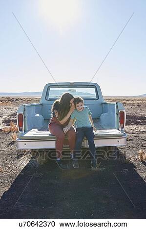 Stock Image - USA, Arizona, Mother with son (6-7) sitting on tailgate of pick-up truck. Fotosearch