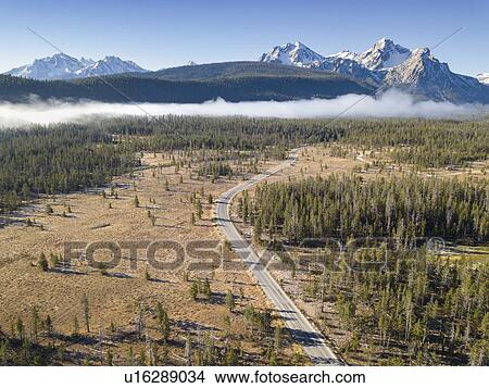 Picture - USA, Idaho, Sawtooth Range, Road in forest with snowcapped mountains in background. Fotosearch