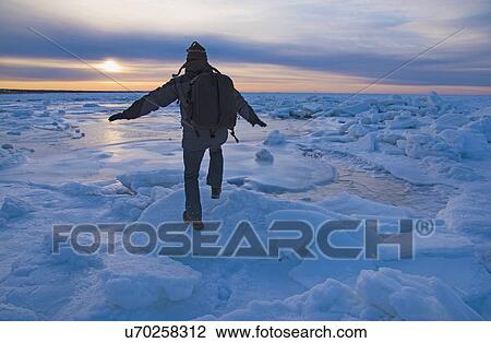 Stock Image - USA, Massachusetts, Cape Cod, Eastham, Man balancing on sea ice at dusk. Fotosearch