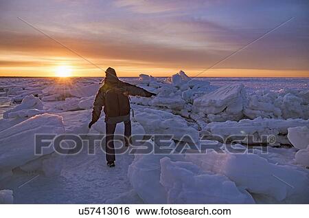 Stock Photograph - USA, Massachusetts, Cape Cod, Eastham, Man balancing on sea ice at dusk. Fotosearch