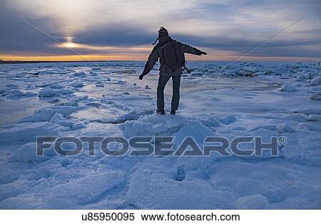 Stock Photography - USA, Massachusetts, Cape Cod, Eastham, Man balancing on sea ice at dusk. Fotosearch