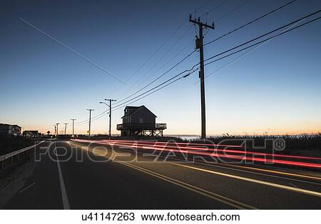 Stock Image - USA, Massachusetts, Cape Cod, Falmouth, Blurred taillight of car on road at dawn. Fotosearch