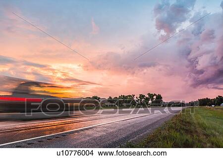 Picture - Vehicle travelling on wet highway at sunset, Montana, US. Fotosearch