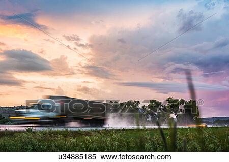Stock Photography - Vehicle travelling on wet highway at sunset, Montana, US. Fotosearch