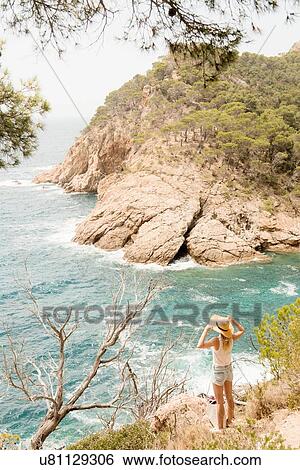 Stock Photograph - Woman along coastline, looking at view, elevated view, Tossa de mar, Catalonia, Spain. Fotosearch