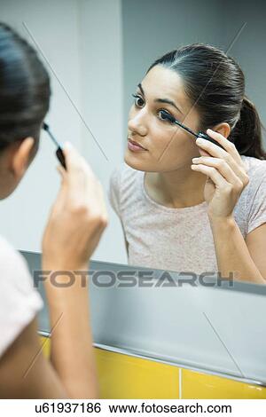 Stock Photograph - Woman applying mascara in front of mirror. Fotosearch