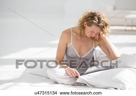 Woman at home, sitting on bed, using laptop View Large Photo Image Picture - Woman at home, sitting on bed, using laptop. Fotosearch