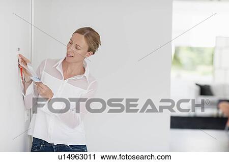 Stock Image - Woman comparing color swatch with white wall. Fotosearch