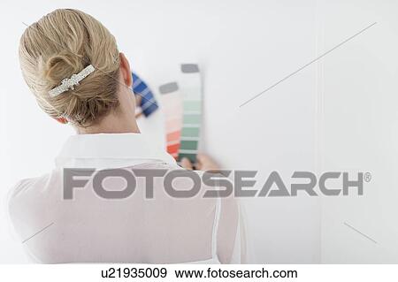 Stock Photo - Woman comparing color swatch with white wall. Fotosearch