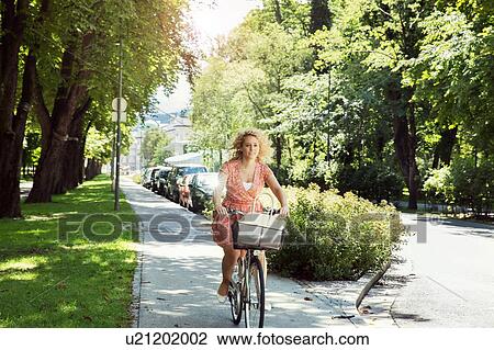 Stock Image - Woman cycling on bicycle in tree lined street, Innsbruck, Tirol, Austria, Europe. Fotosearch