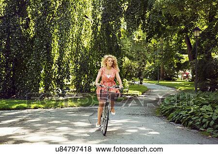 Woman cycling on bicycle through park View Large Photo Image Stock Photo - Woman cycling on bicycle through park. Fotosearch
