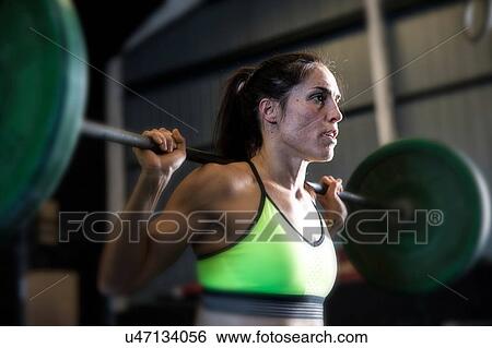 Stock Photograph - Woman exercising in gym, using barbell. Fotosearch