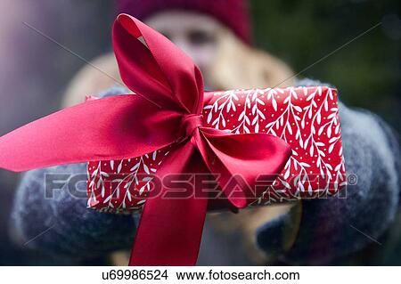 Picture - Woman holding up Christmas present with red ribbon. Fotosearch