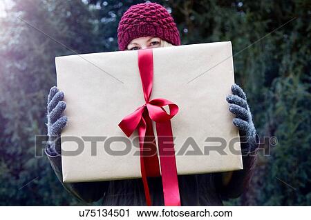 Stock Image - Woman holding up Christmas present with red ribbon. Fotosearch